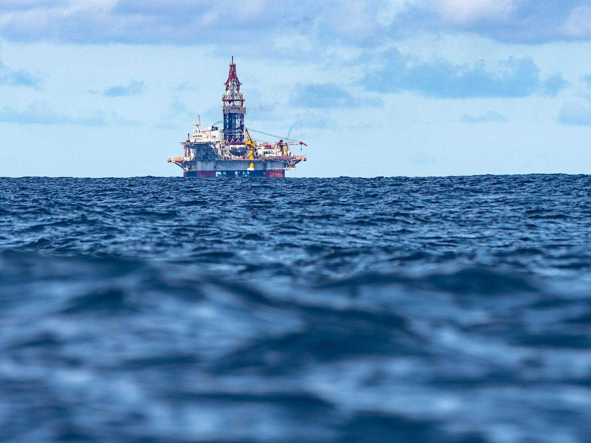 A drilling platform on the horizon of a dark blue, choppy sea under a partly cloudy sky