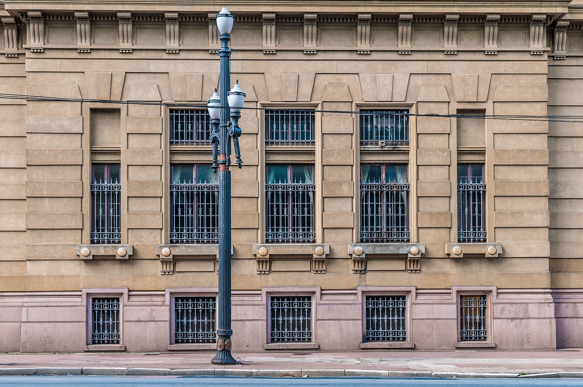 The sandstone side facade of the Palacio da Justica in Sao Paulo, with barred windows and a black iron street lamp in front