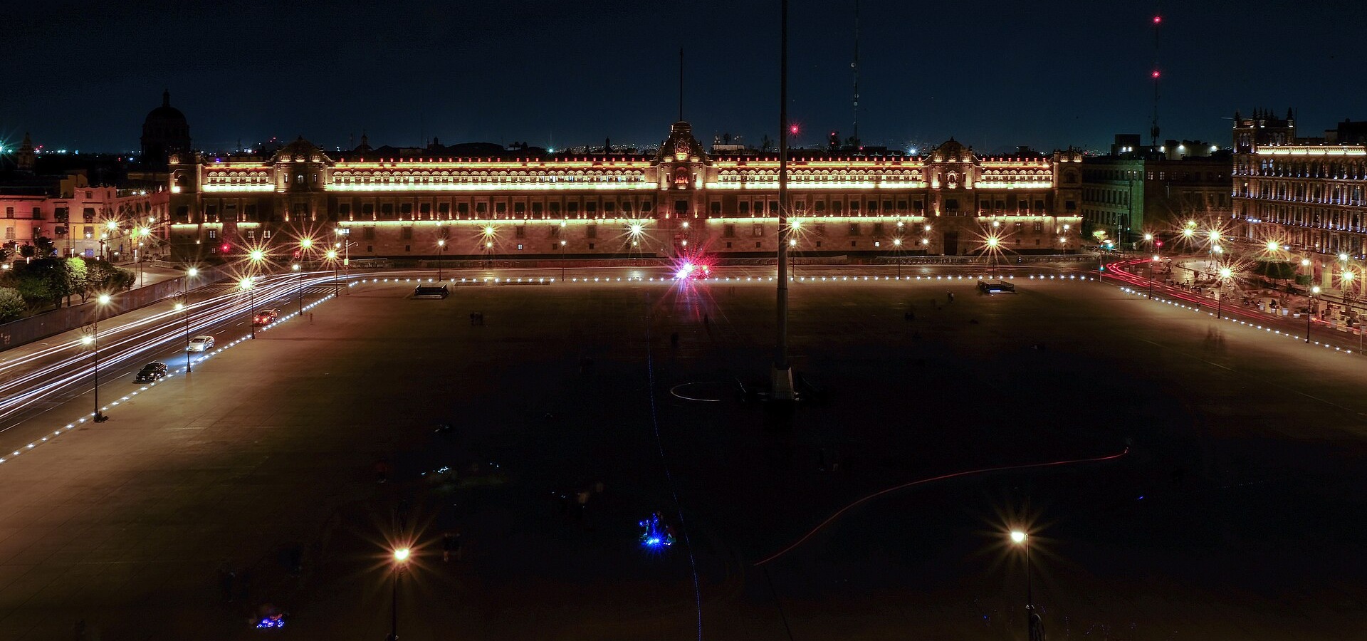 Palacio Nacional in Mexico City lit up at night, a long low palace facade behind the empty Zocalo square with a tall flagpole