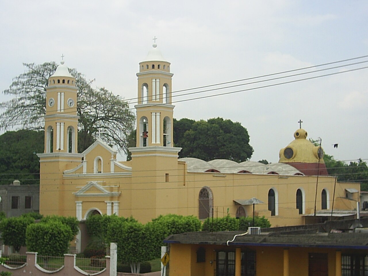 A yellow and white church with two bell towers and a yellow dome under a cloudy sky in Tuxtepec