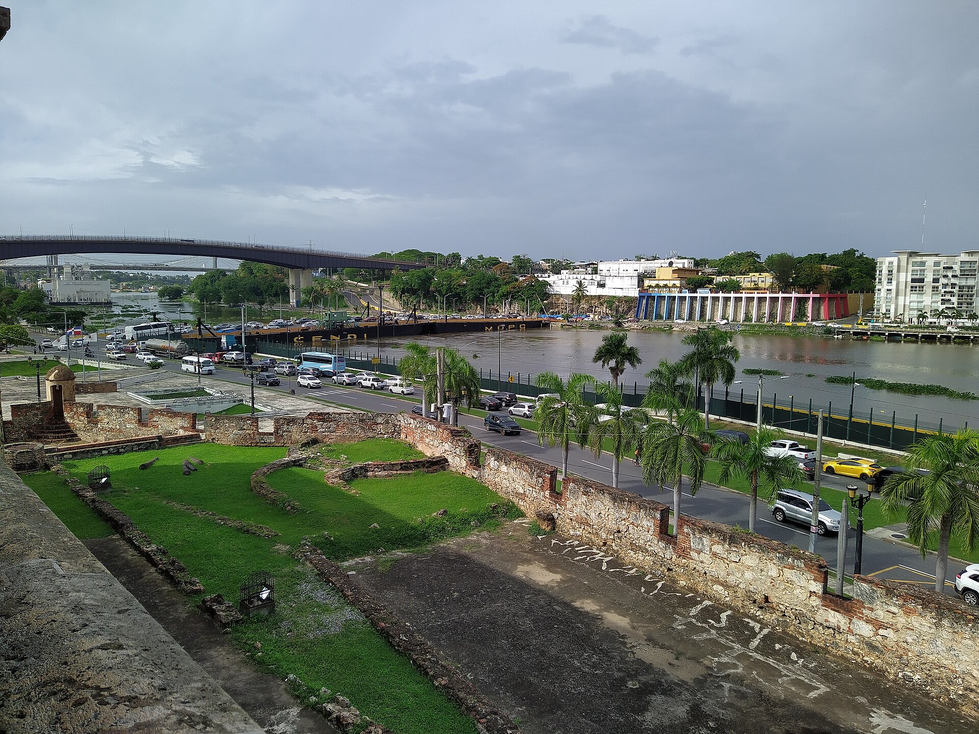 The Ozama River under a grey sky seen from the stone walls of the Alcazar de Colon, with road bridges crossing the water in the distance