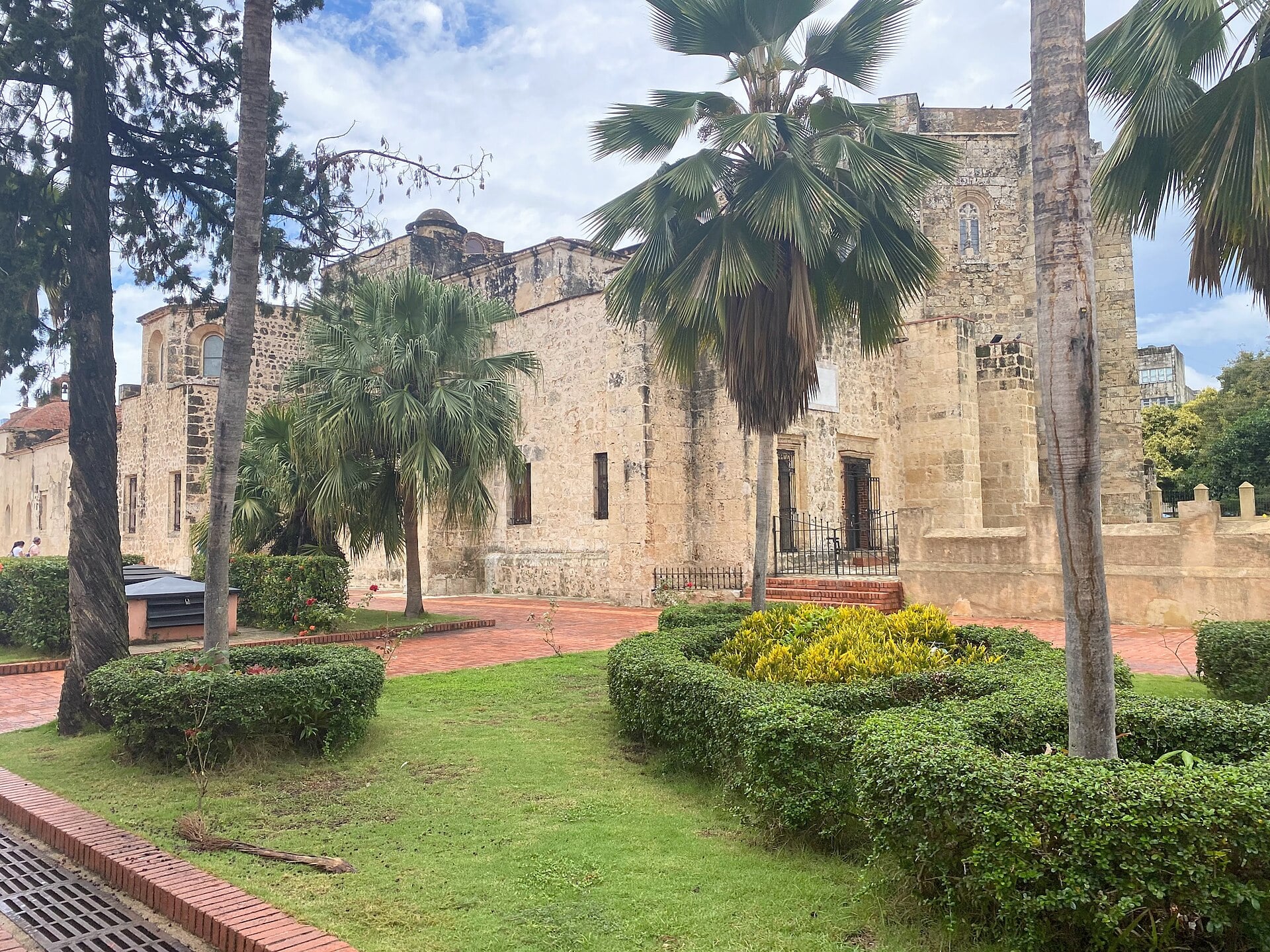 Stone walls and side entrance of the Primatial Cathedral behind palms and clipped hedges in Santo Domingo's Colonial City