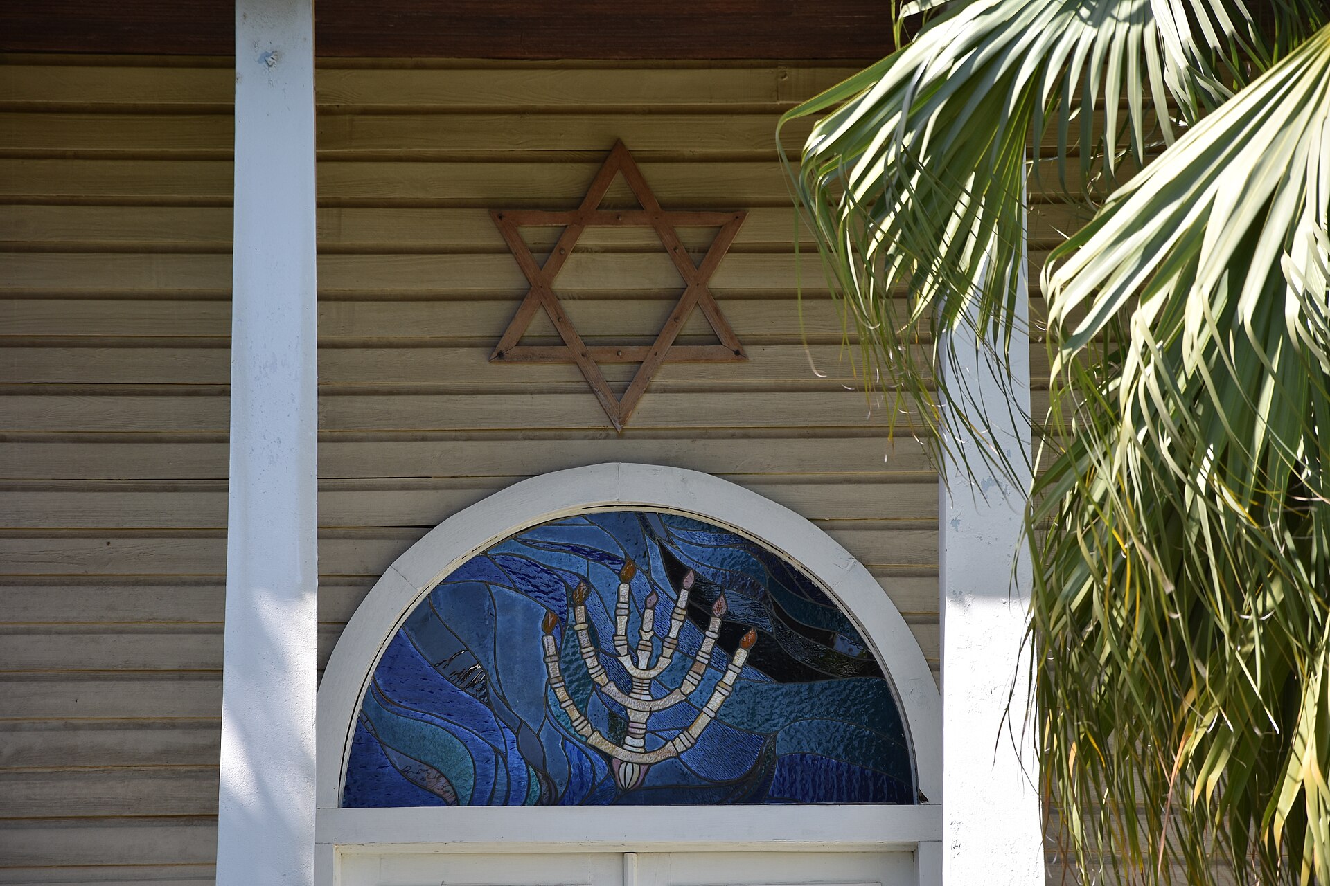 Wooden facade of a synagogue with a Star of David and a stained-glass menorah under an arched window