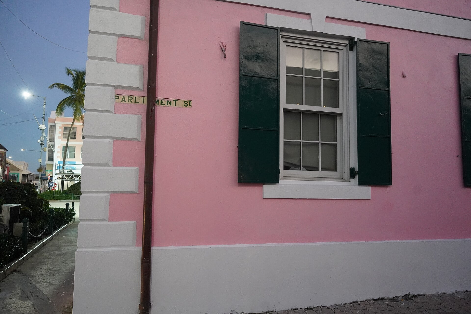 Pink colonial wall with green shutters and a Parliament Street sign beside the House of Assembly in downtown Nassau