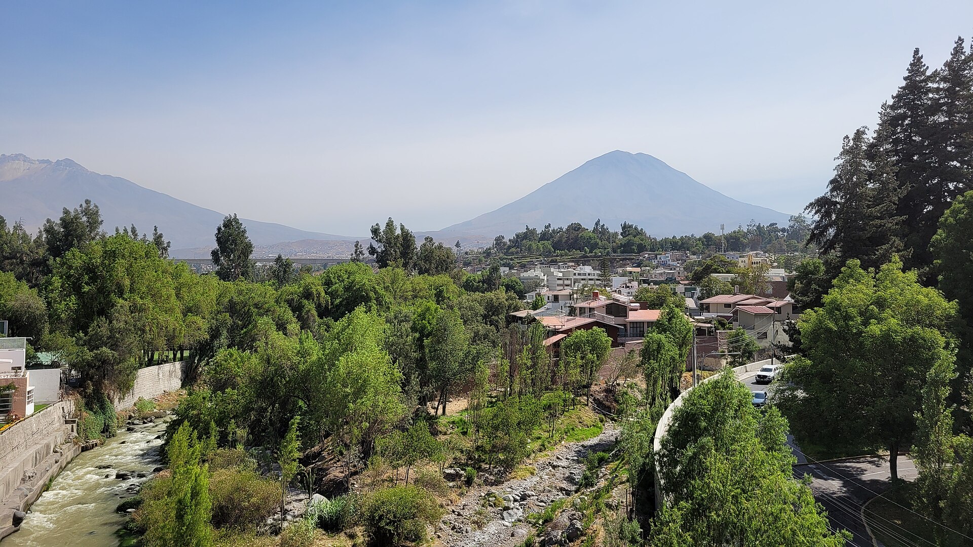 The conical El Misti volcano rising above houses, trees and a rocky river channel in the southern Peruvian city of Arequipa
