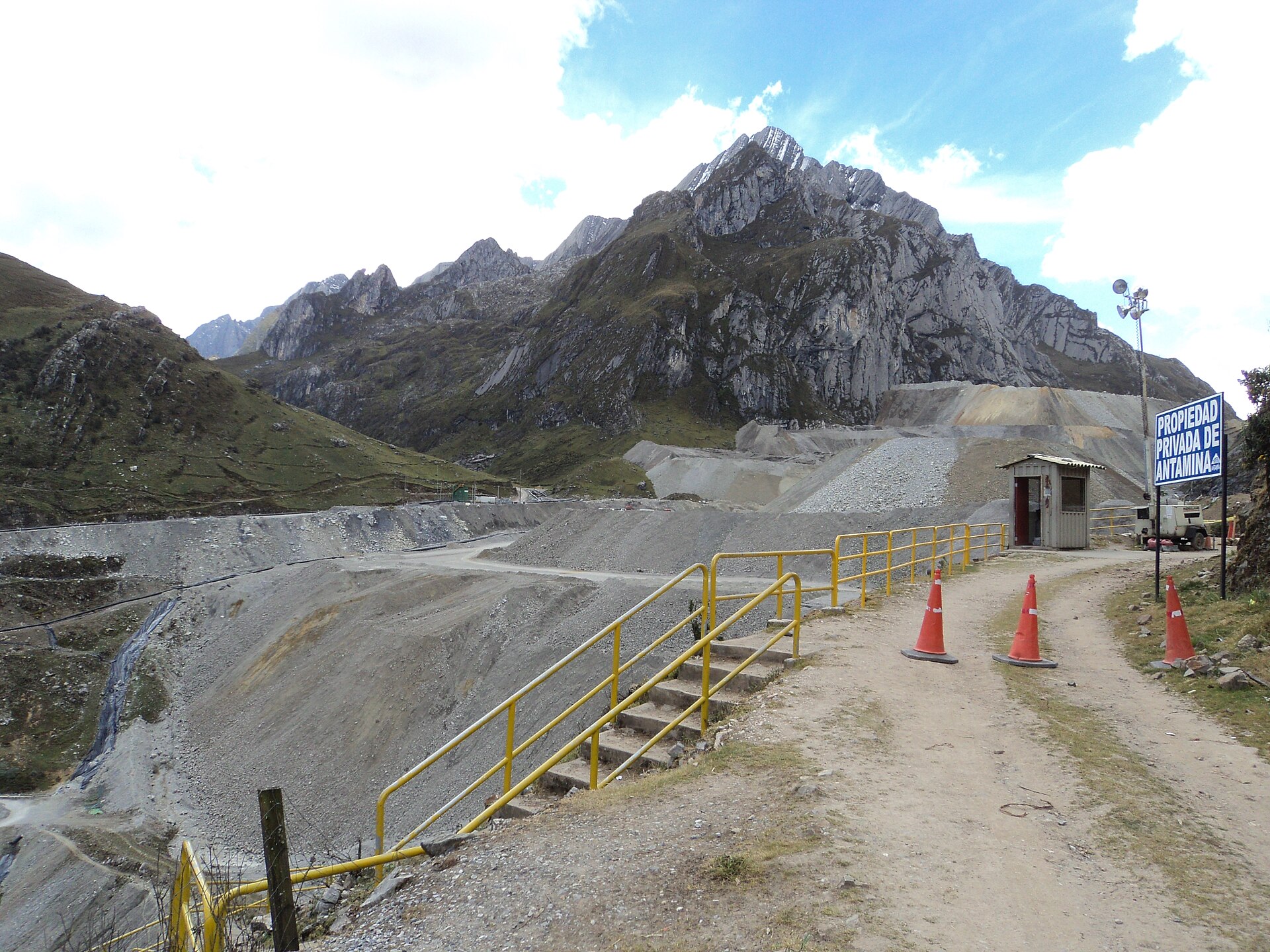 Gravel waste dump, yellow railings, traffic cones and a sign reading Propiedad Privada de Antamina below rocky Andean peaks