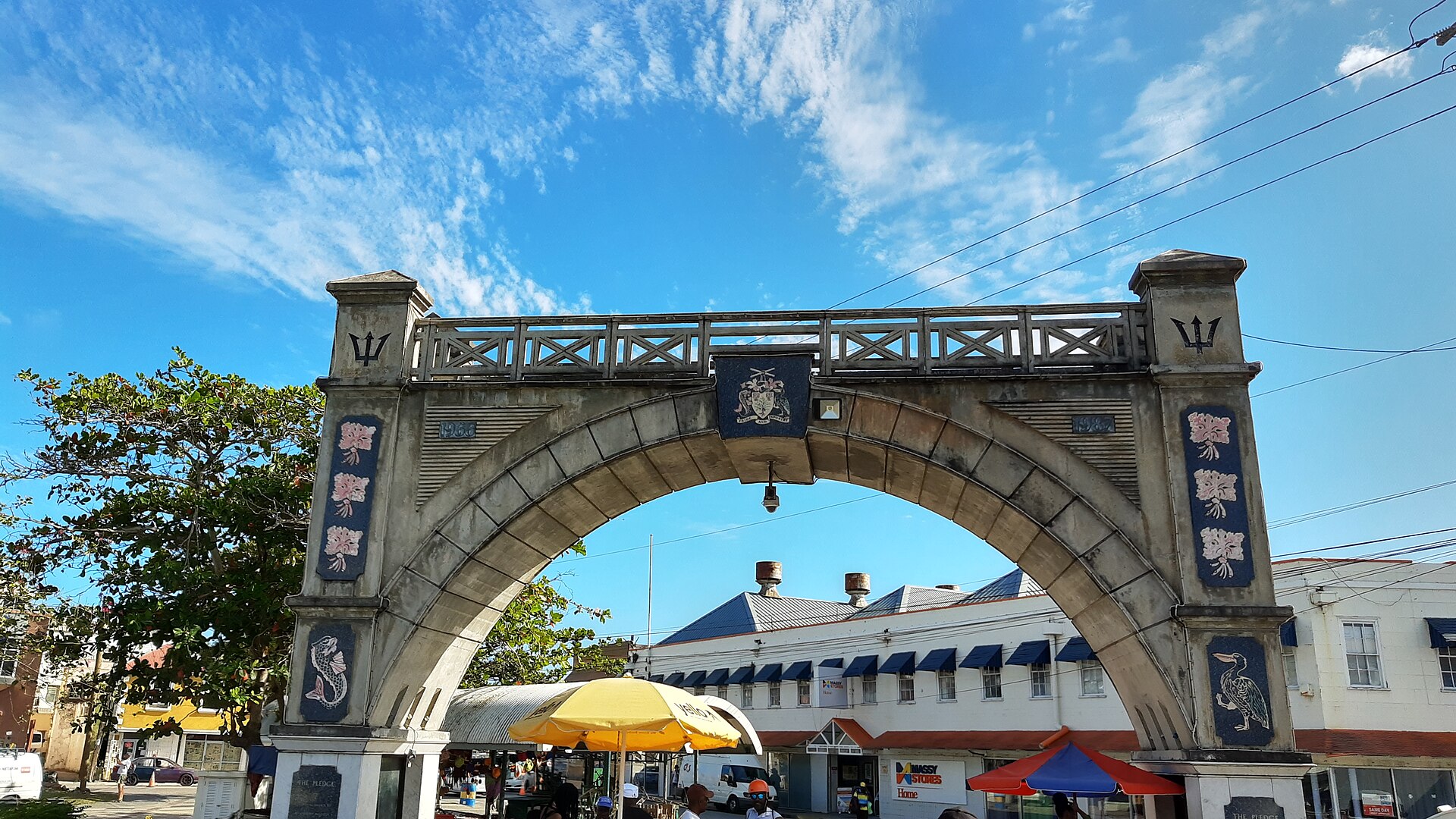 The stone Independence Arch in Bridgetown carrying the Barbados coat of arms, with market stalls and umbrellas beneath it
