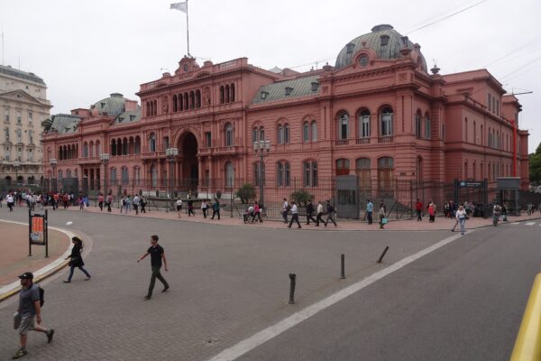 The pink Casa Rosada presidential palace in Buenos Aires seen from Plaza de Mayo, with pedestrians crossing the street in front