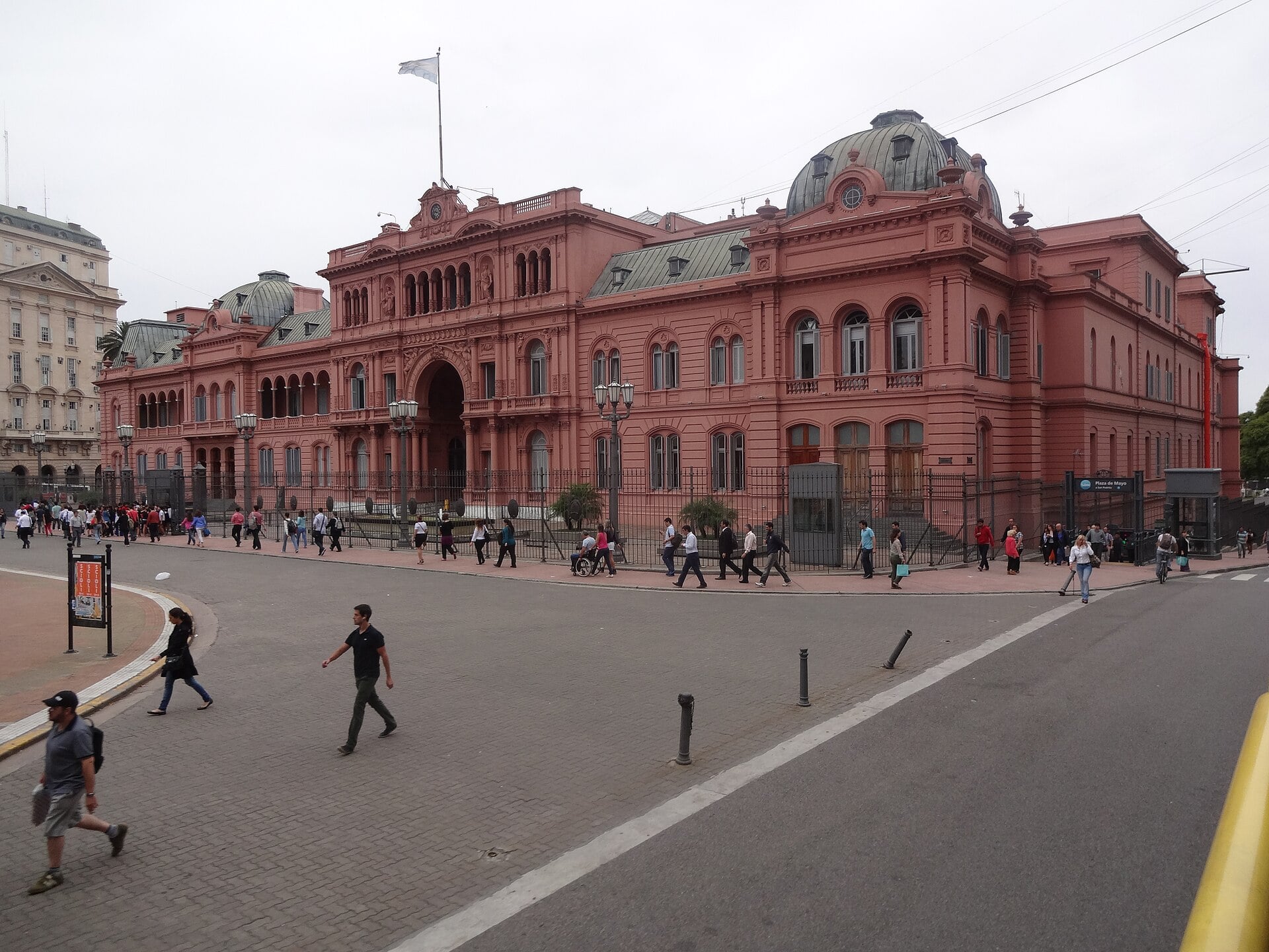 The pink Casa Rosada presidential palace in Buenos Aires seen from Plaza de Mayo, with pedestrians crossing the street in front