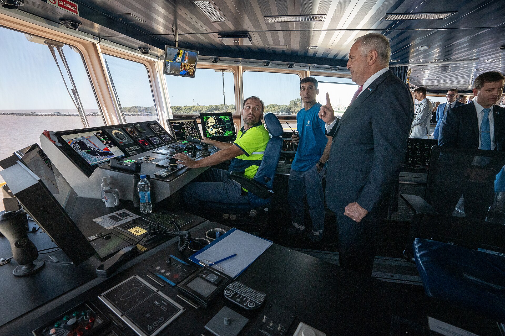 Officials in suits stand on the bridge of a ship at the port of Buenos Aires while a crew member sits at the navigation console