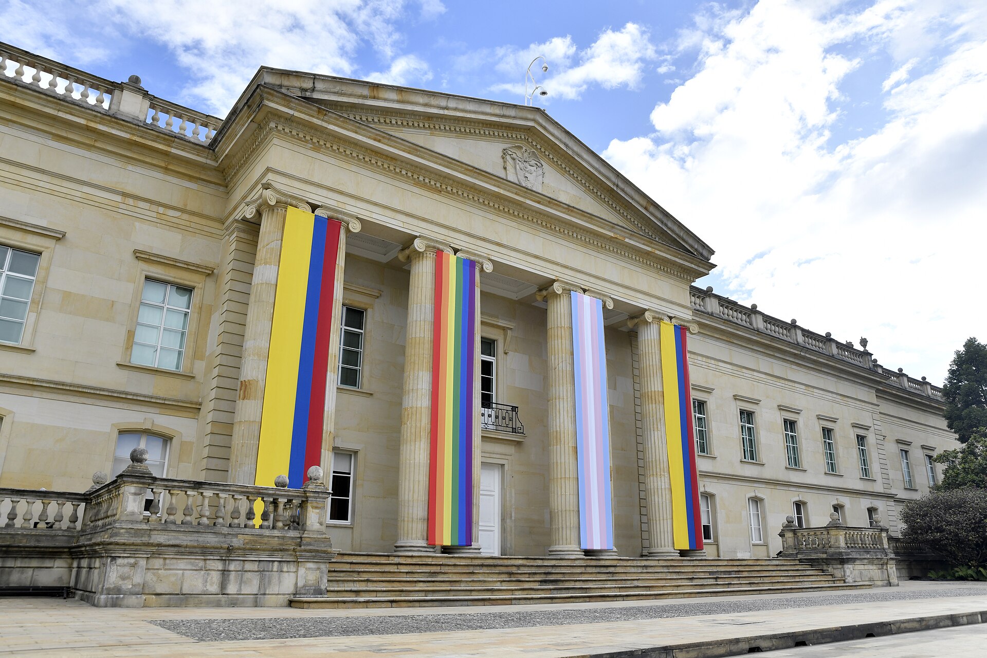 The columned front of the Casa de Nariño presidential palace in Bogotá, with tall banners in the Colombian national colours and rainbow and transgender-pride colours hanging between the columns