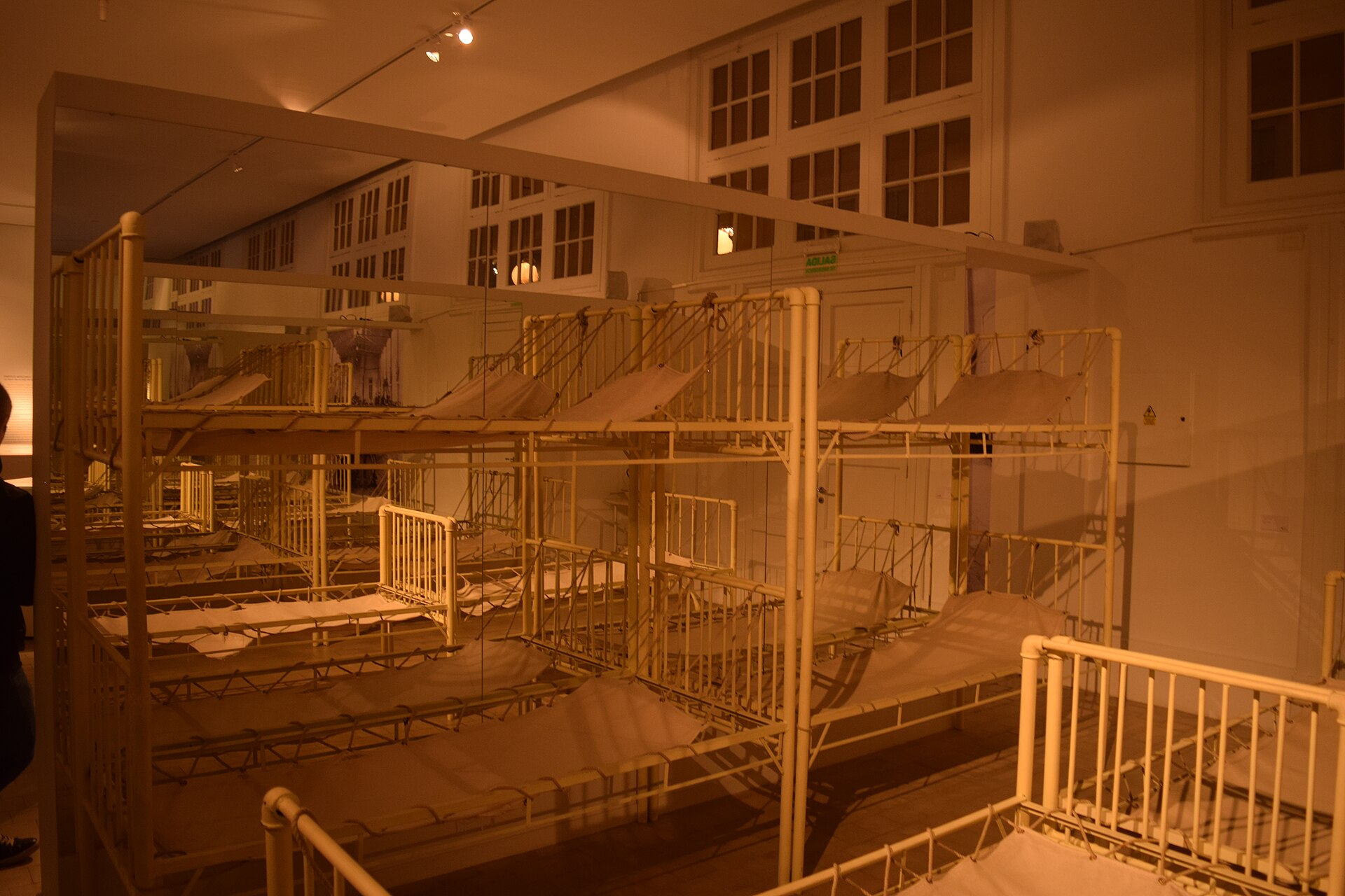 Rows of white metal bunk beds with canvas bases in a dimly lit hall of the immigration museum in Buenos Aires