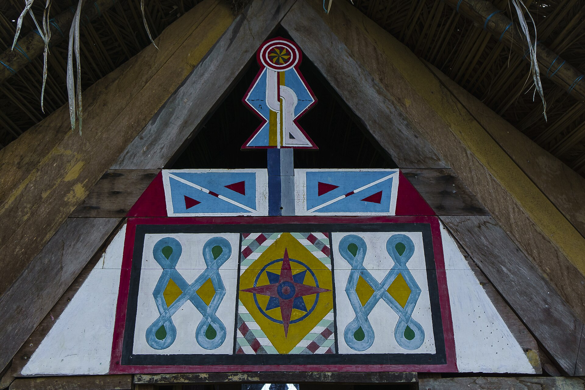 A painted wooden gable in red, blue, yellow and white with geometric Maroon designs and a compass-star motif under a thatched roof
