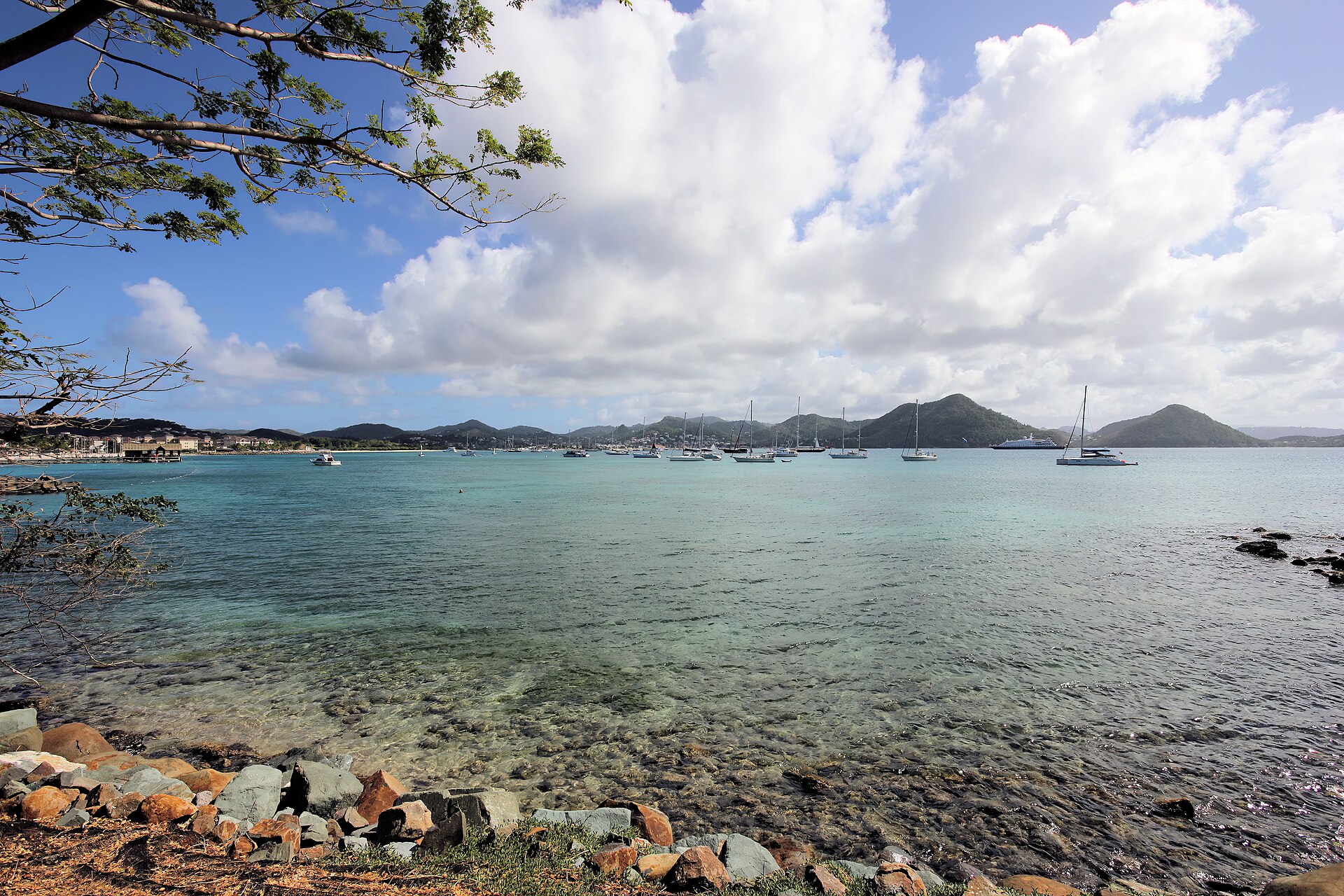 Turquoise water of Rodney Bay with sailing yachts at anchor and green hills across the bay under big clouds