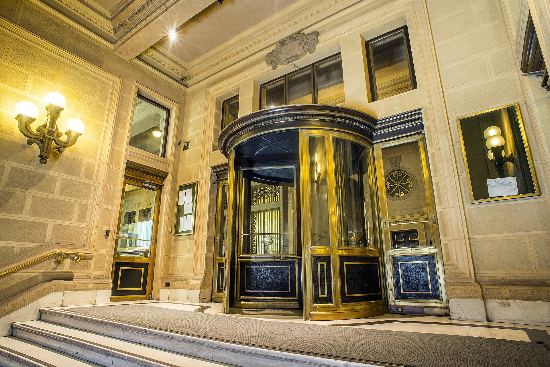 Stone entrance hall with a brass revolving door, wall lamps and marble steps inside the Banco Central de Chile