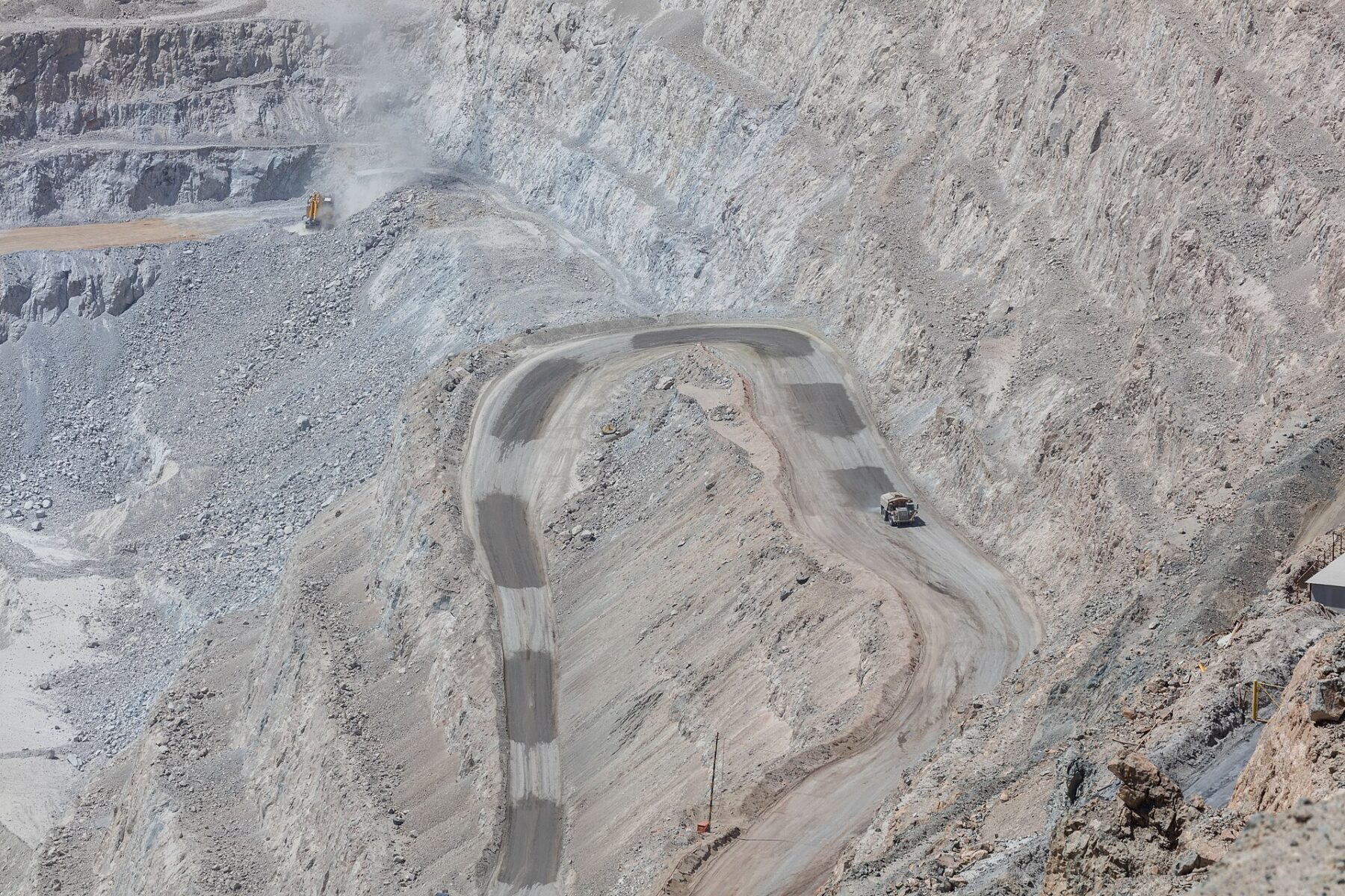 A haul truck climbs a switchback ramp cut into the grey terraced walls of a vast open-pit copper mine
