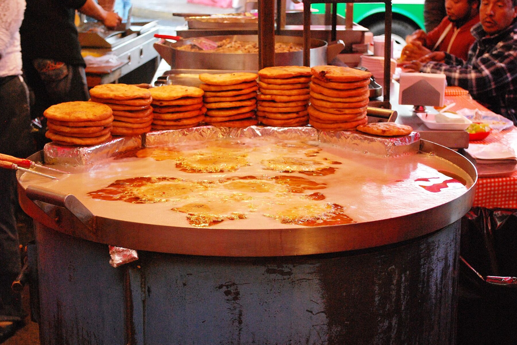 Stacks of golden gorditas beside a wide steel pan of hot oil at a street food stand in Mexico City