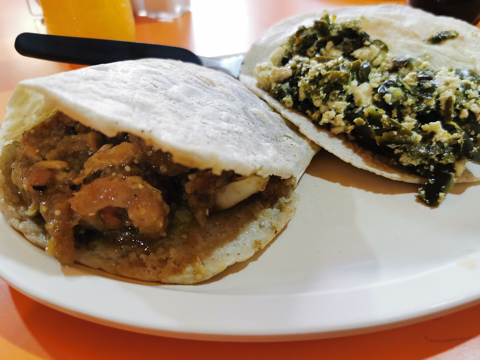 Two corn gorditas on a white plate, one stuffed with pork crackling in green salsa and one with green chilli strips