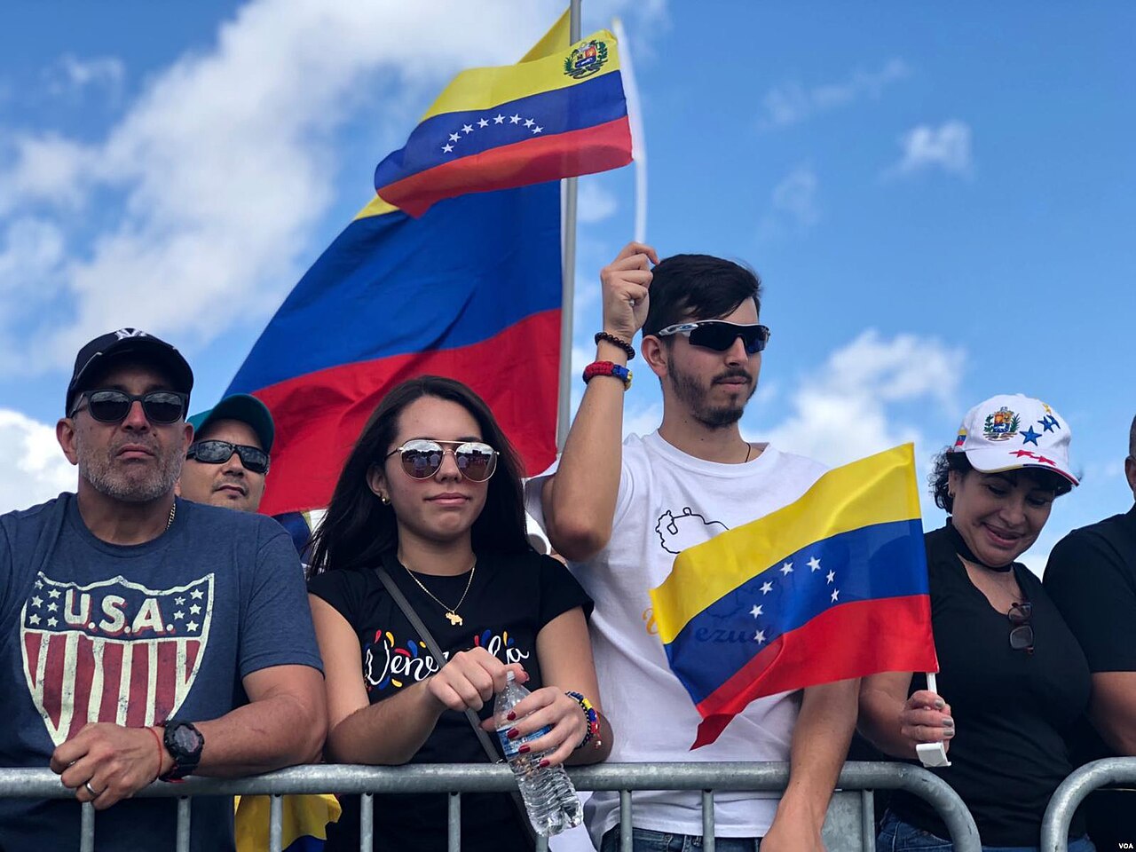 Venezuelan Americans holding Venezuelan flags behind a metal barrier at an outdoor rally in Florida