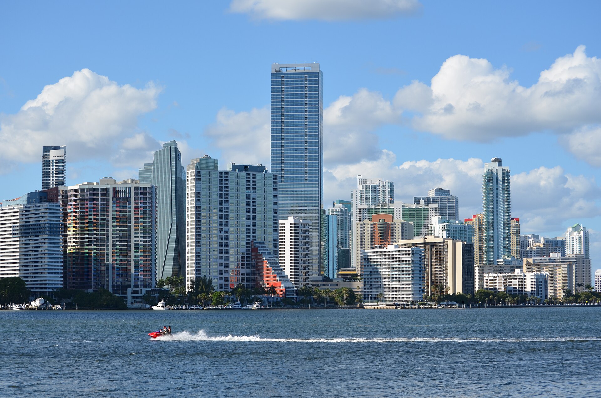 High-rise apartment and office towers of Brickell, Miami, across blue water under a partly cloudy sky, with a jet ski in the foreground