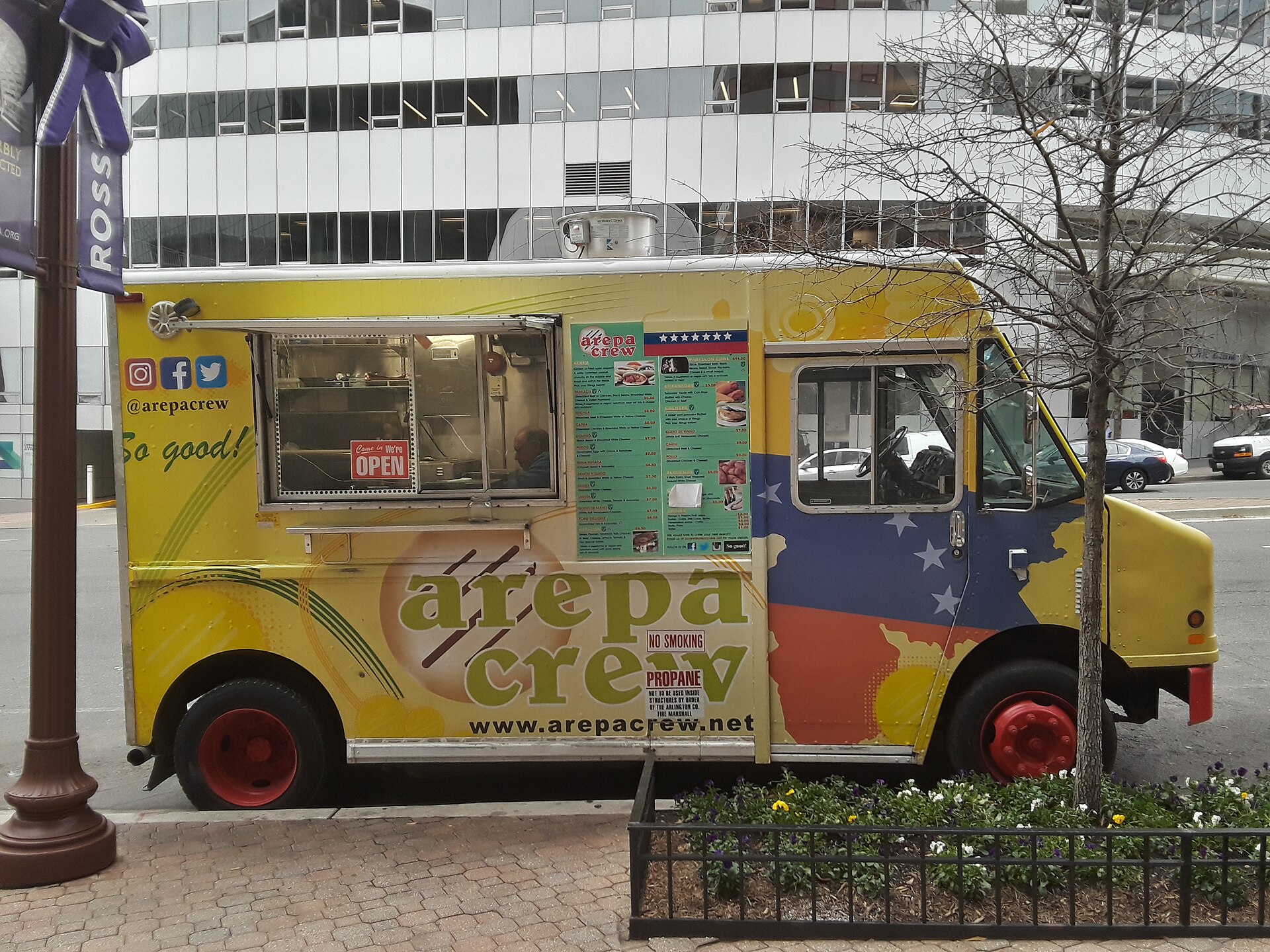 A yellow food truck painted with the Venezuelan flag colours and the name Arepa Crew parked on a city street
