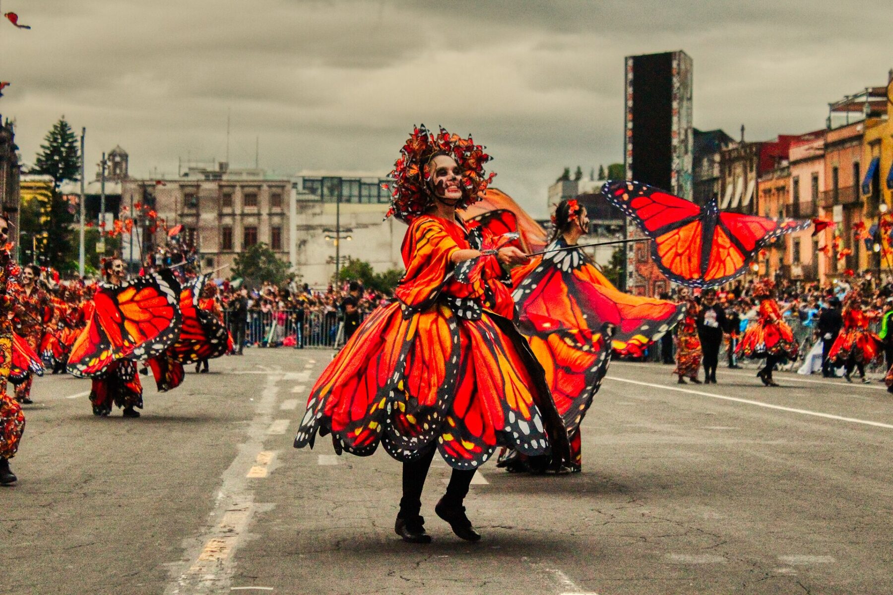 Dancers in orange monarch-butterfly costumes and skull face paint perform on a Mexico City avenue lined with spectators