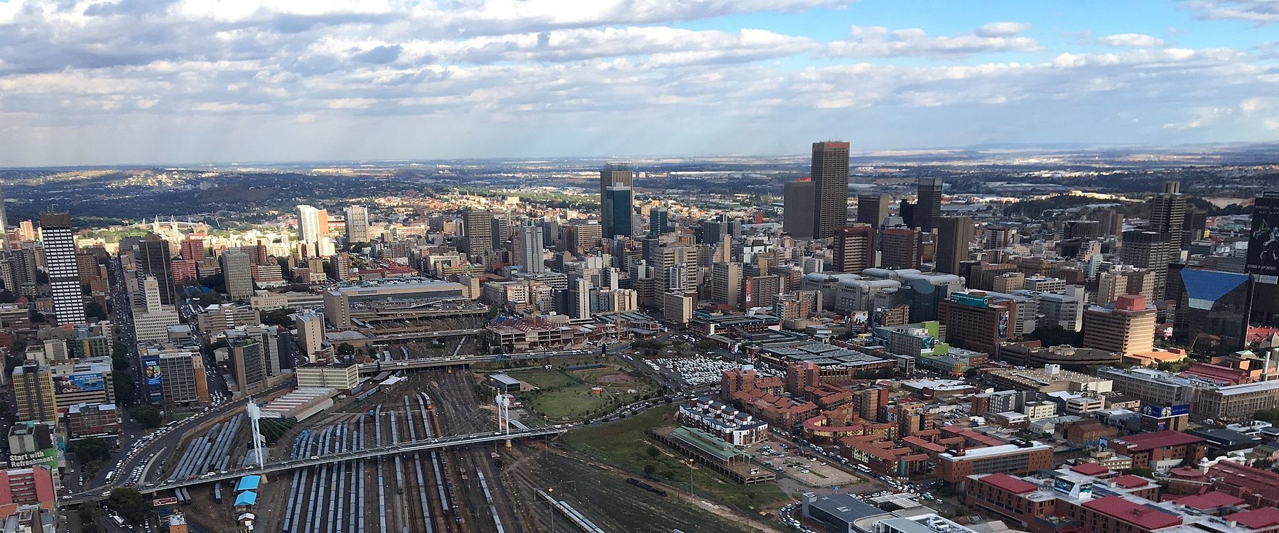 Aerial view of central Johannesburg's office towers with railway yards in the foreground under a partly cloudy sky
