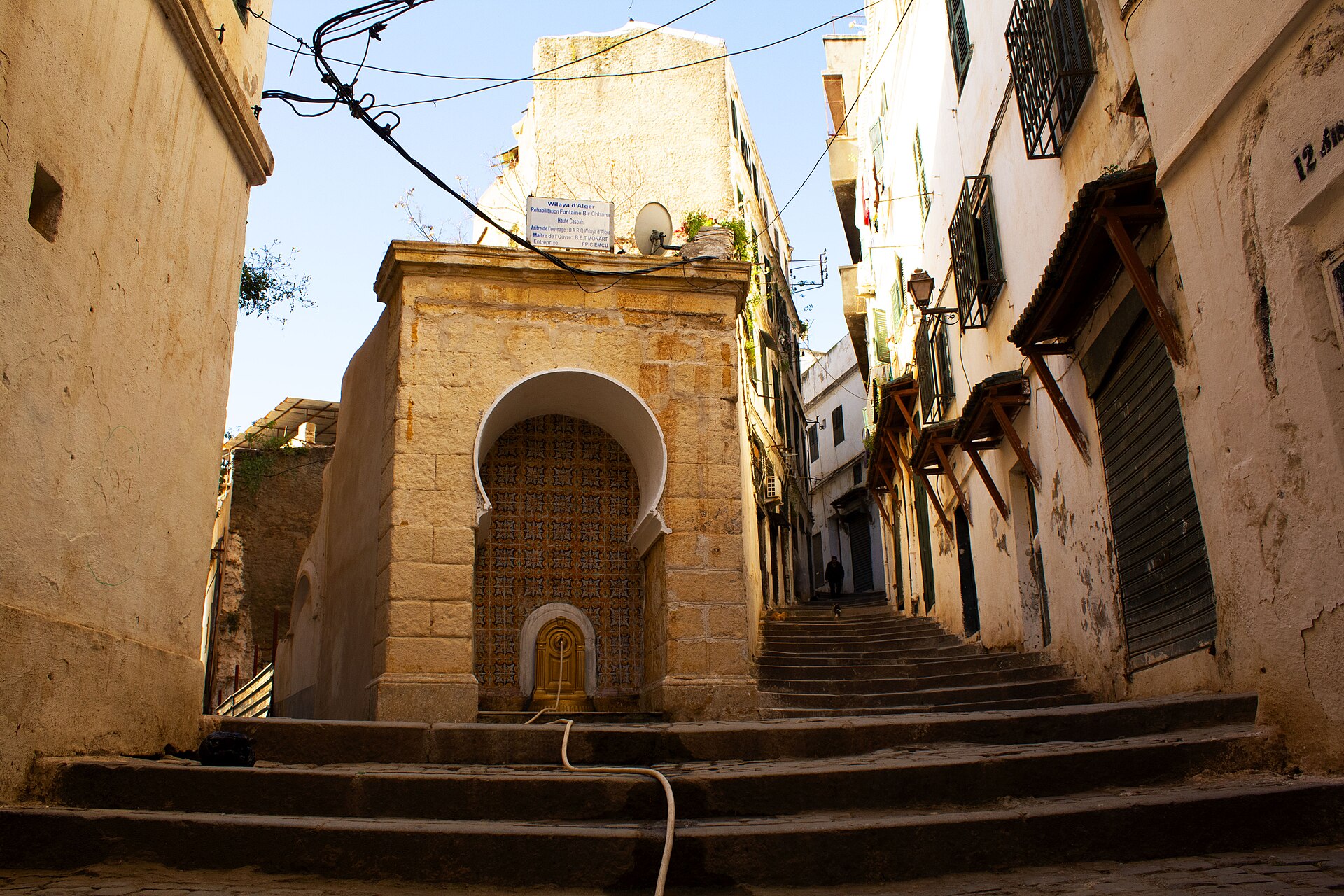 A stone fountain with a tiled niche at the top of a stepped lane between whitewashed houses in the Casbah of Algiers