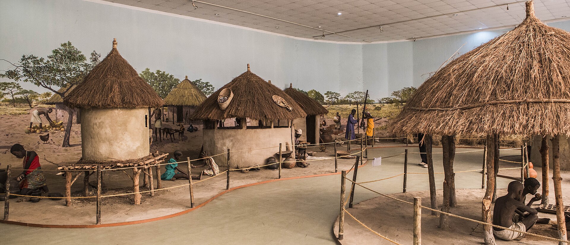 Thatched round huts and figures in a village diorama inside a museum hall