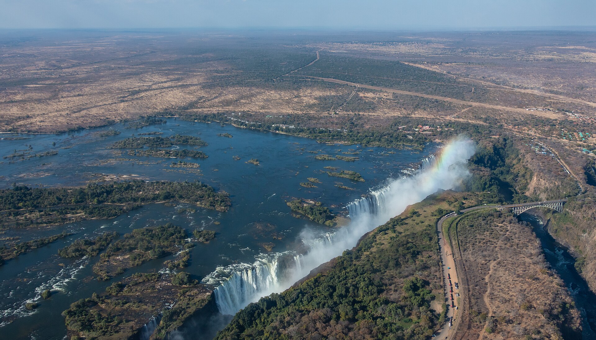 Aerial view of Victoria Falls with spray and a rainbow above the gorge and a bridge on the right