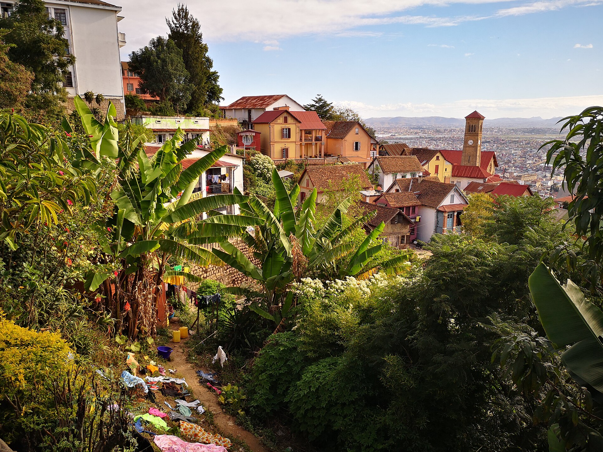 Houses with red roofs and a church tower on a green hillside in Antananarivo, with the city spread out under a blue sky