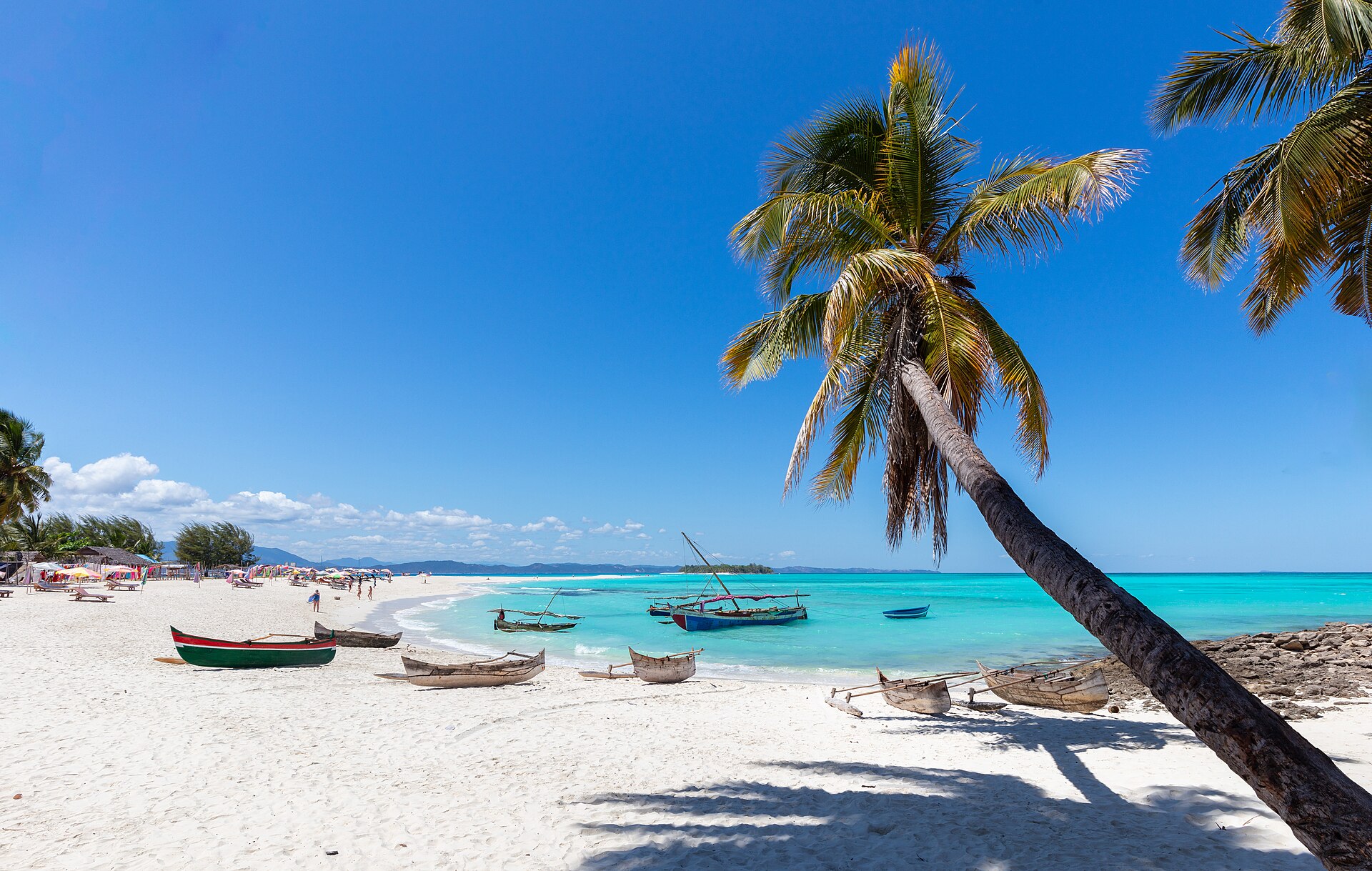 White sand beach with a leaning coconut palm, turquoise water and wooden outrigger boats on Nosy Iranja island