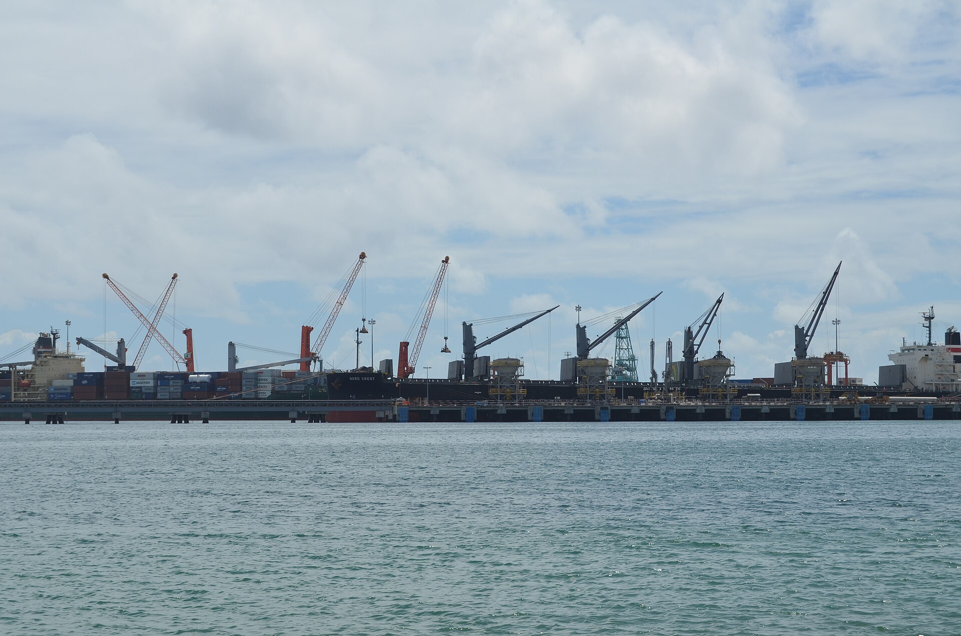Cargo ships with cranes and stacked containers moored at a quay in the port of Toamasina seen across calm water