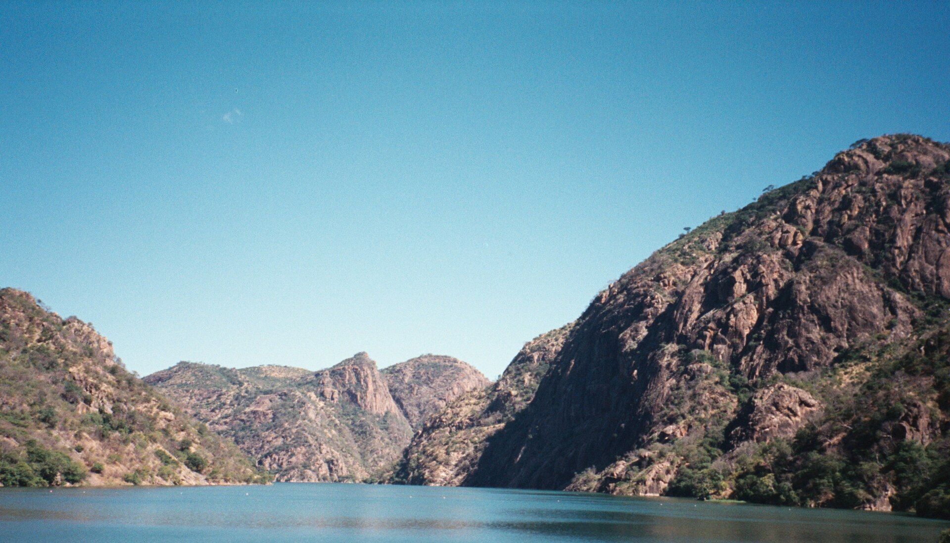 A narrow blue reservoir between steep rocky brown hills under a clear blue sky in the Cahora Bassa gorge on the Zambezi river