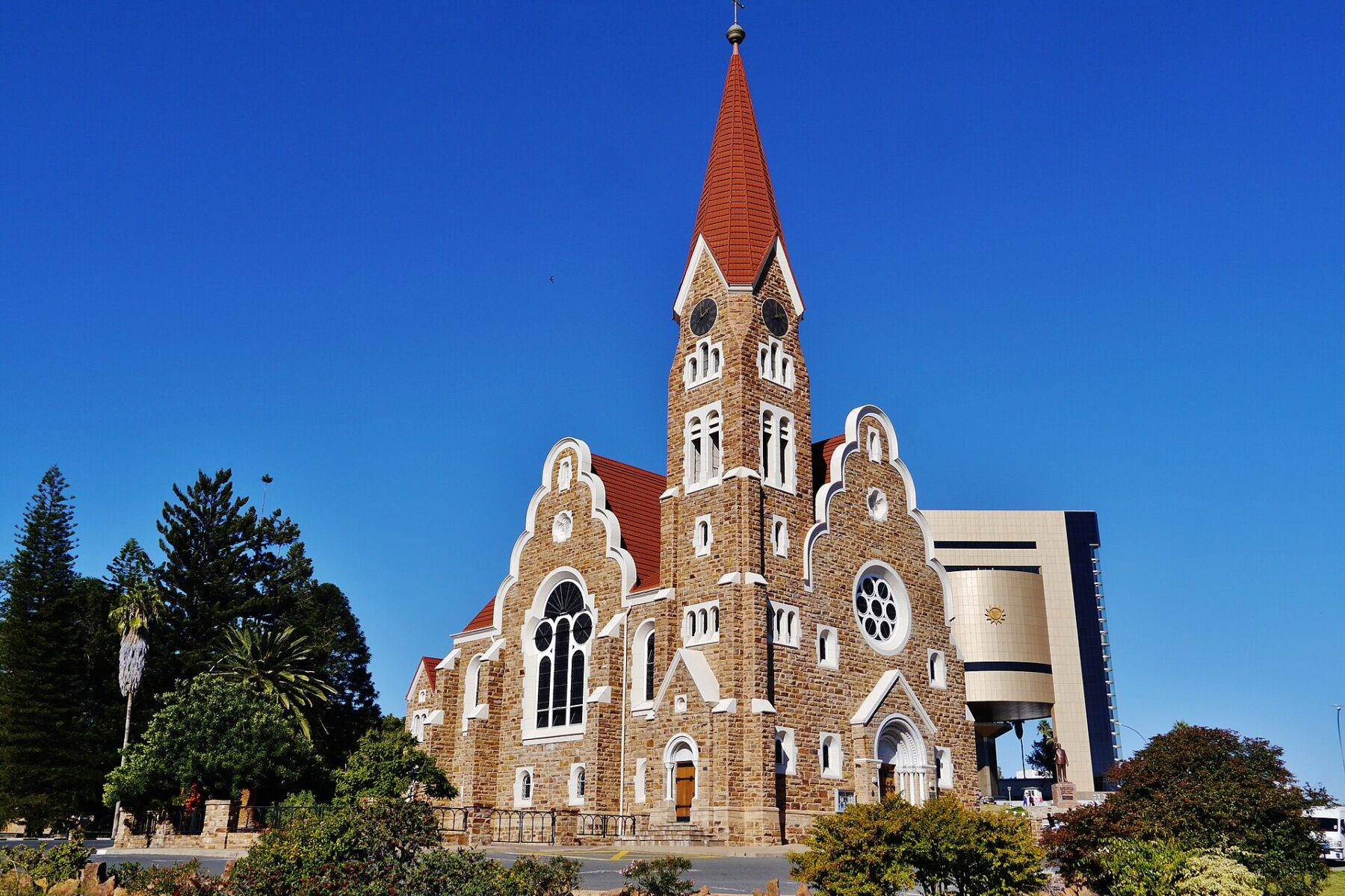 Christ Church in Windhoek, a stone Lutheran church with a red tiled spire, beside the Independence Memorial Museum under a clear blue sky