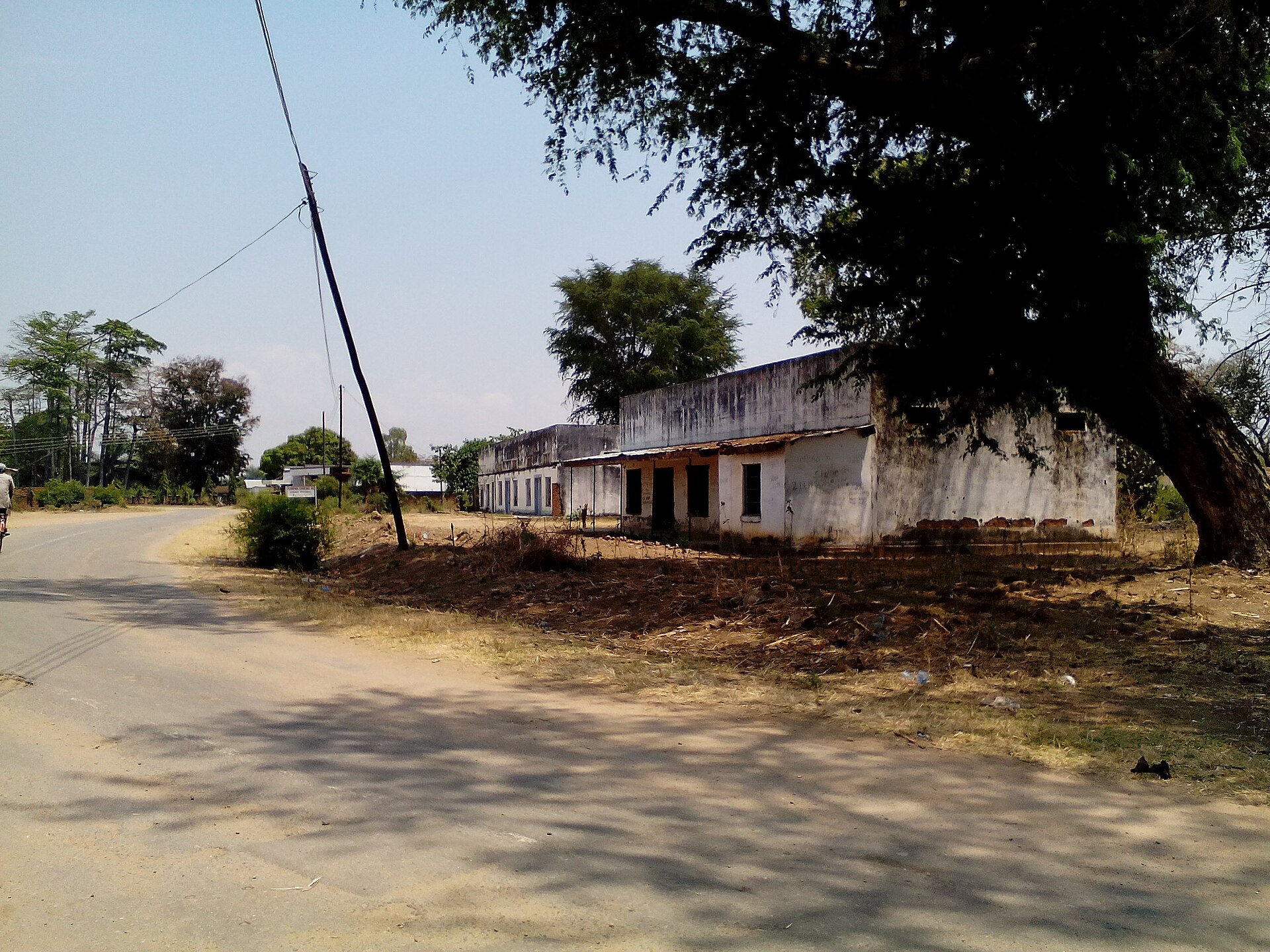 A dirt-edged road with low whitewashed buildings and large trees in the old town of Karonga, northern Malawi