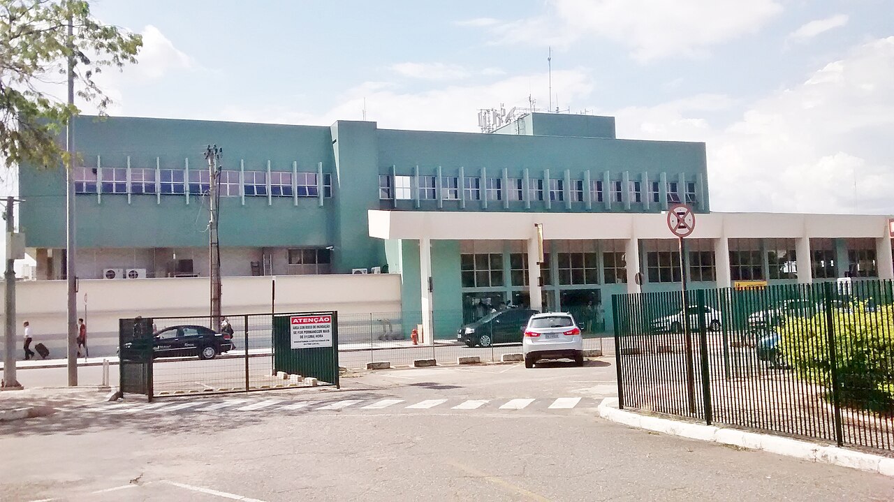 Green and white passenger terminal building of Pampulha Airport seen from the street, with cars parked in front