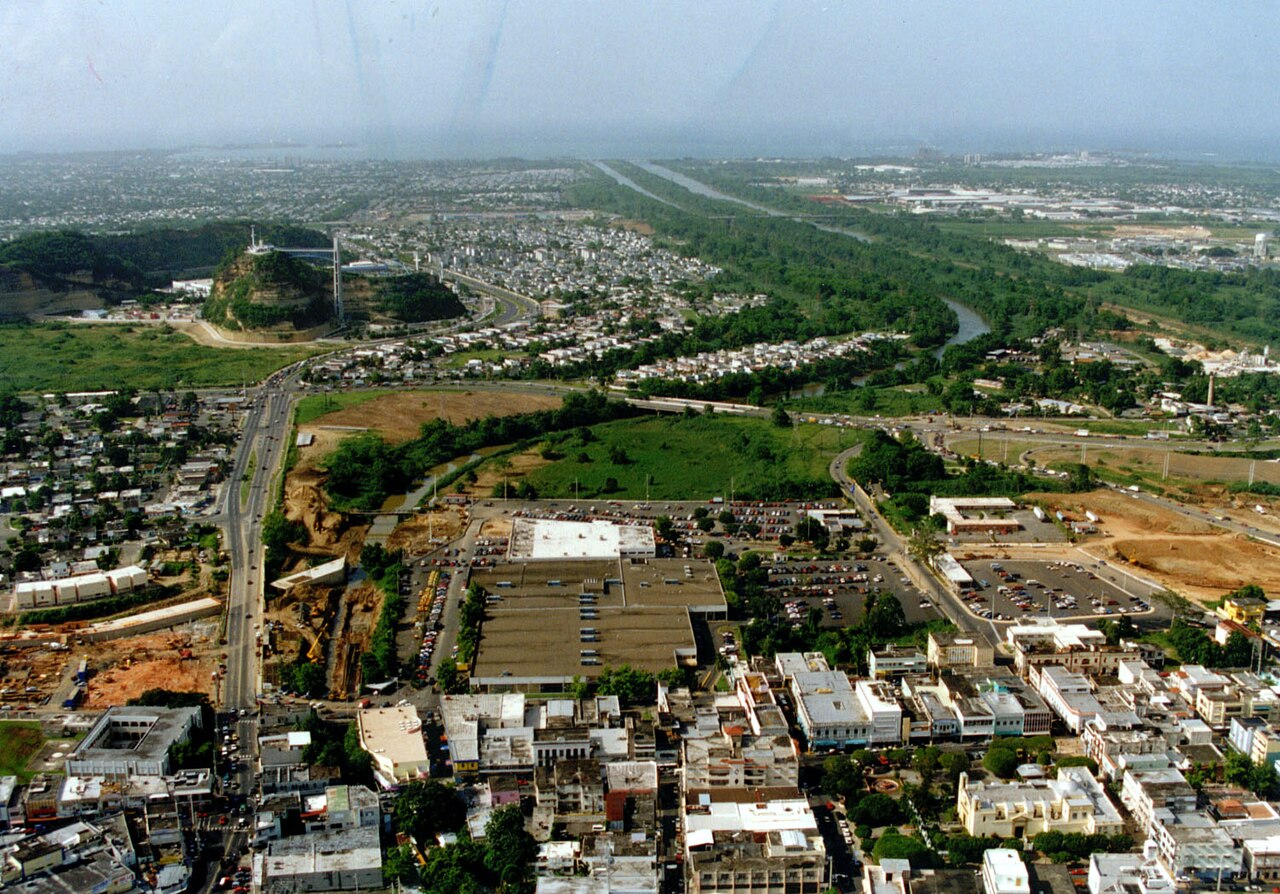 Aerial view of Bayamón, Puerto Rico, with dense streets, a large flat-roofed building and the Bayamón River channel running north towards the coast