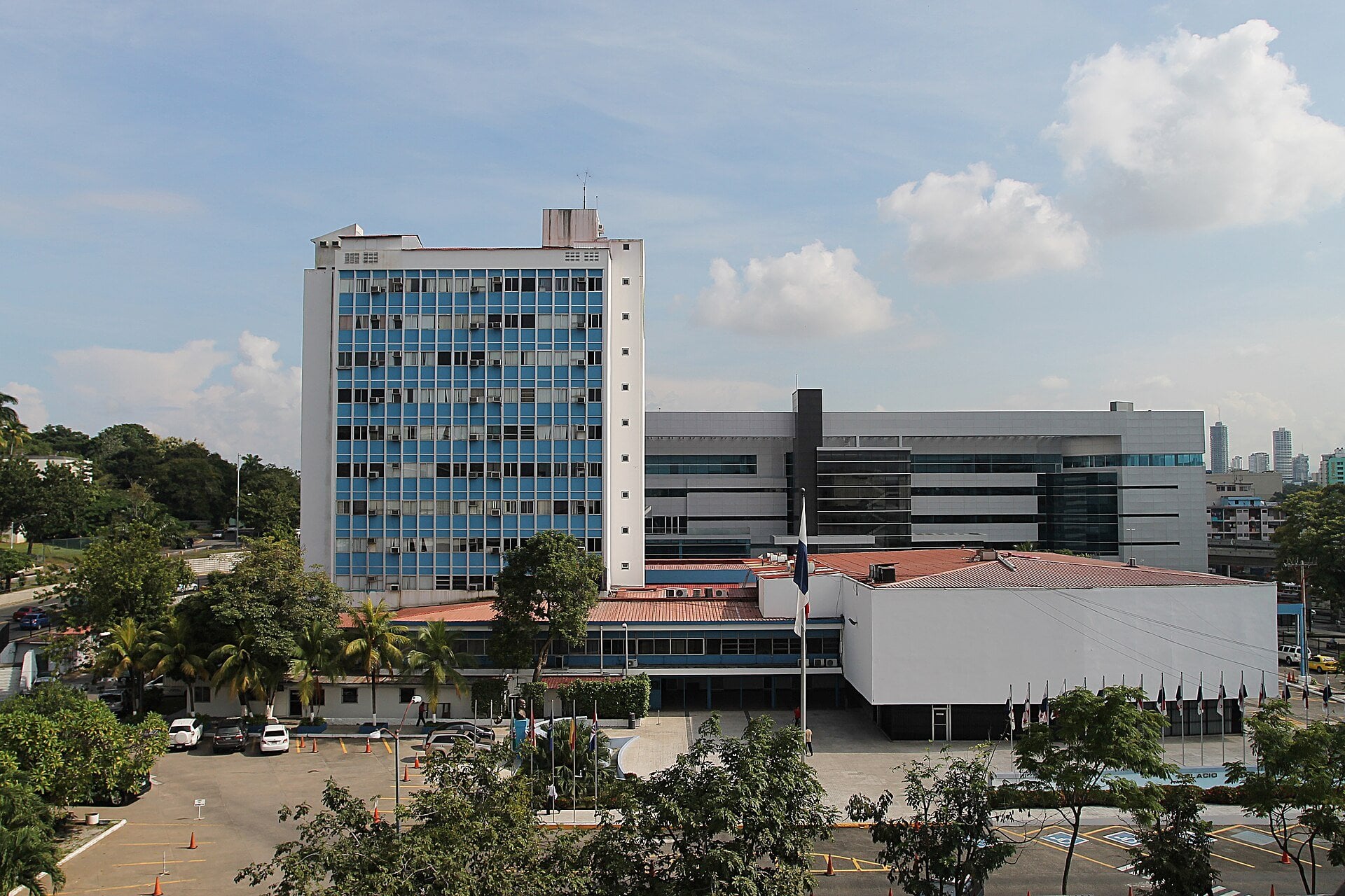 The blue-and-white tower and low annex of Panama's National Assembly complex in Panama City under a partly cloudy sky