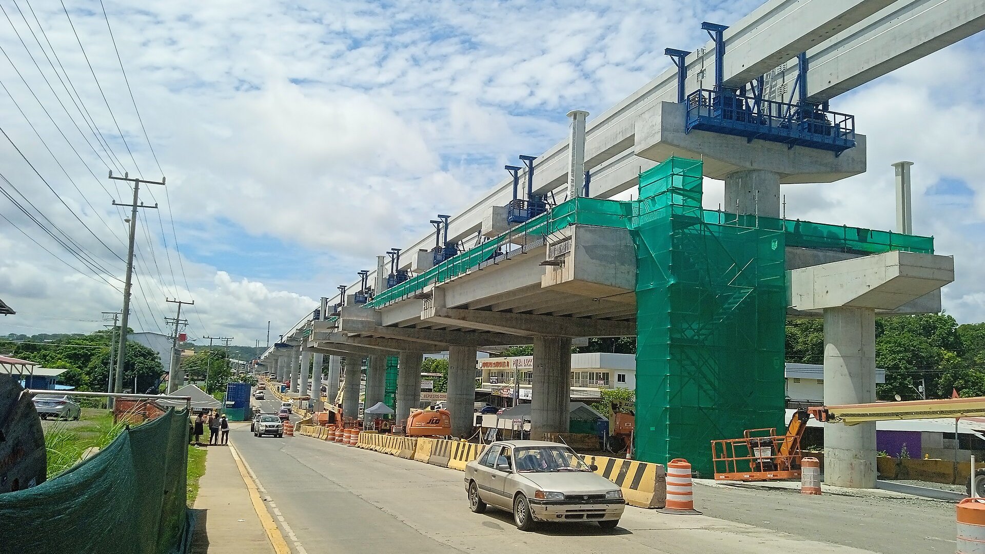 Elevated concrete guideway of Panama Metro Line 3 under construction beside a road in Arraiján with a car and traffic barriers