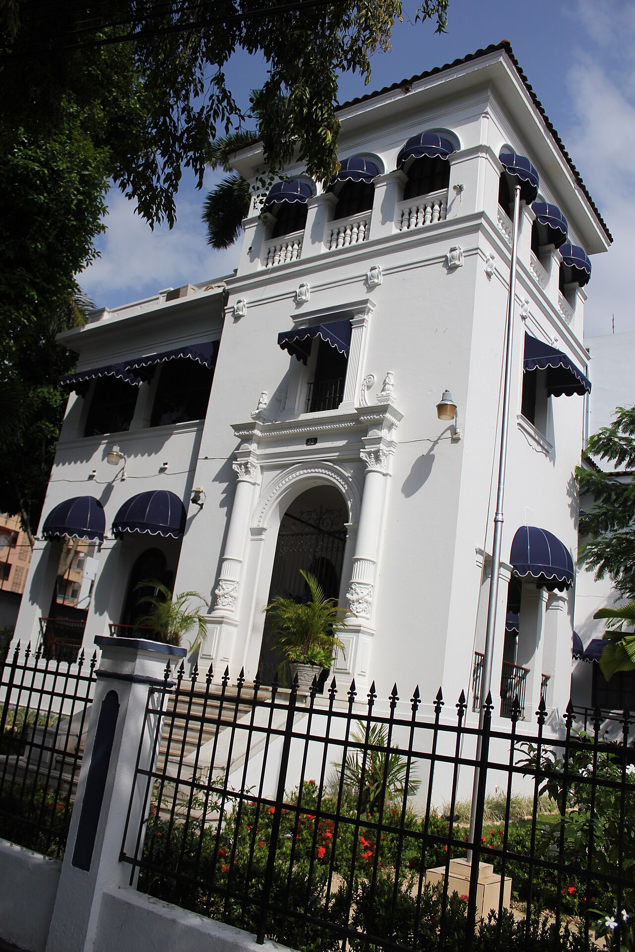 A white colonial-style building with navy awnings behind a black iron fence, home of the Attorney General's Office in Panama City