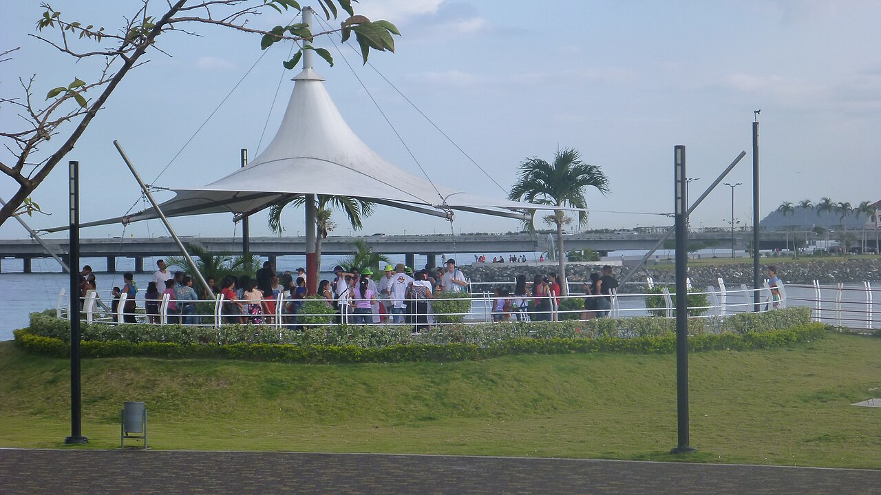 People gather under a white canopy at a lookout point on the Cinta Costera in Panama City, with a coastal bridge behind