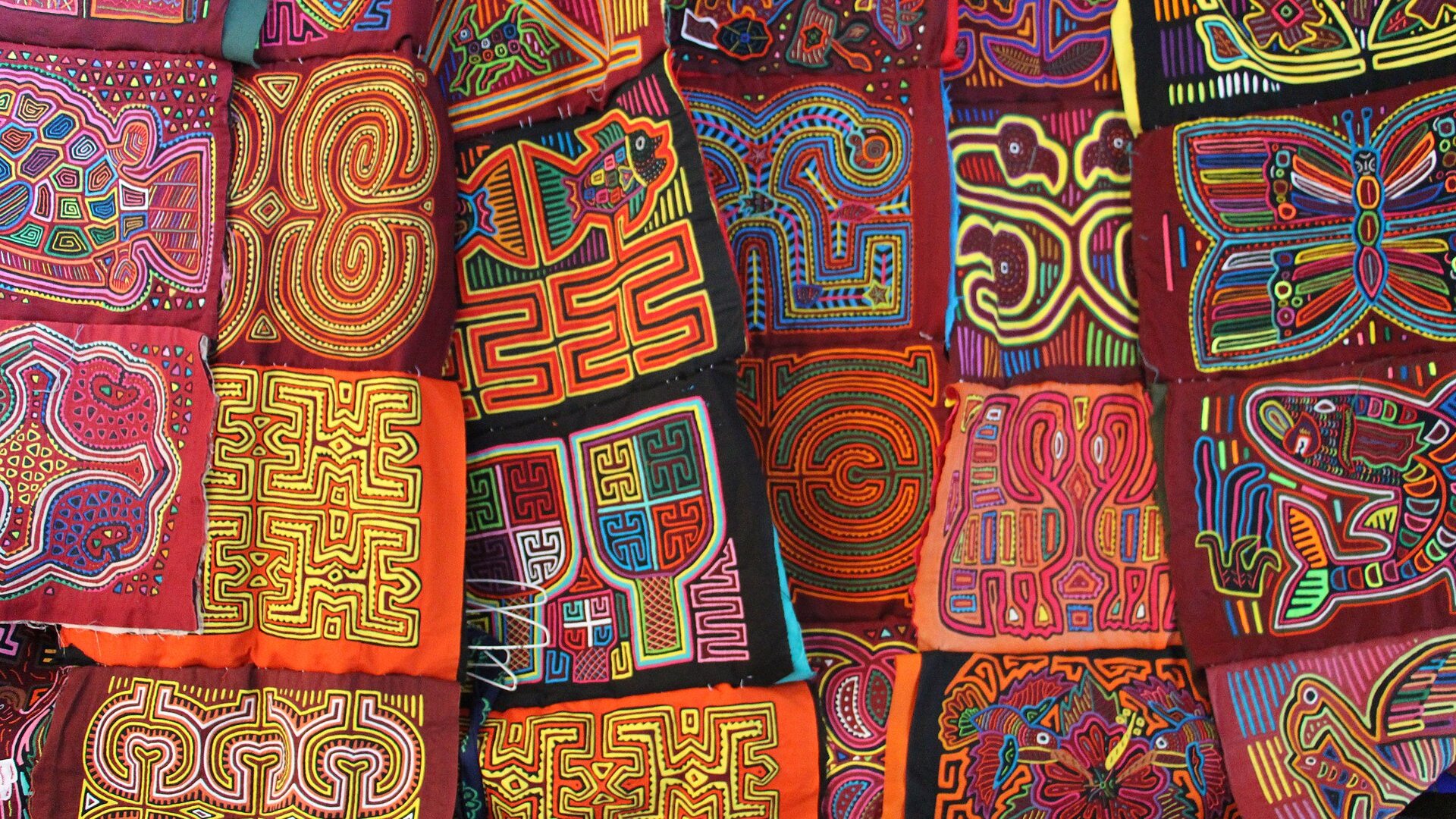 Colourful hand-sewn Guna mola textile panels with geometric and animal patterns laid side by side