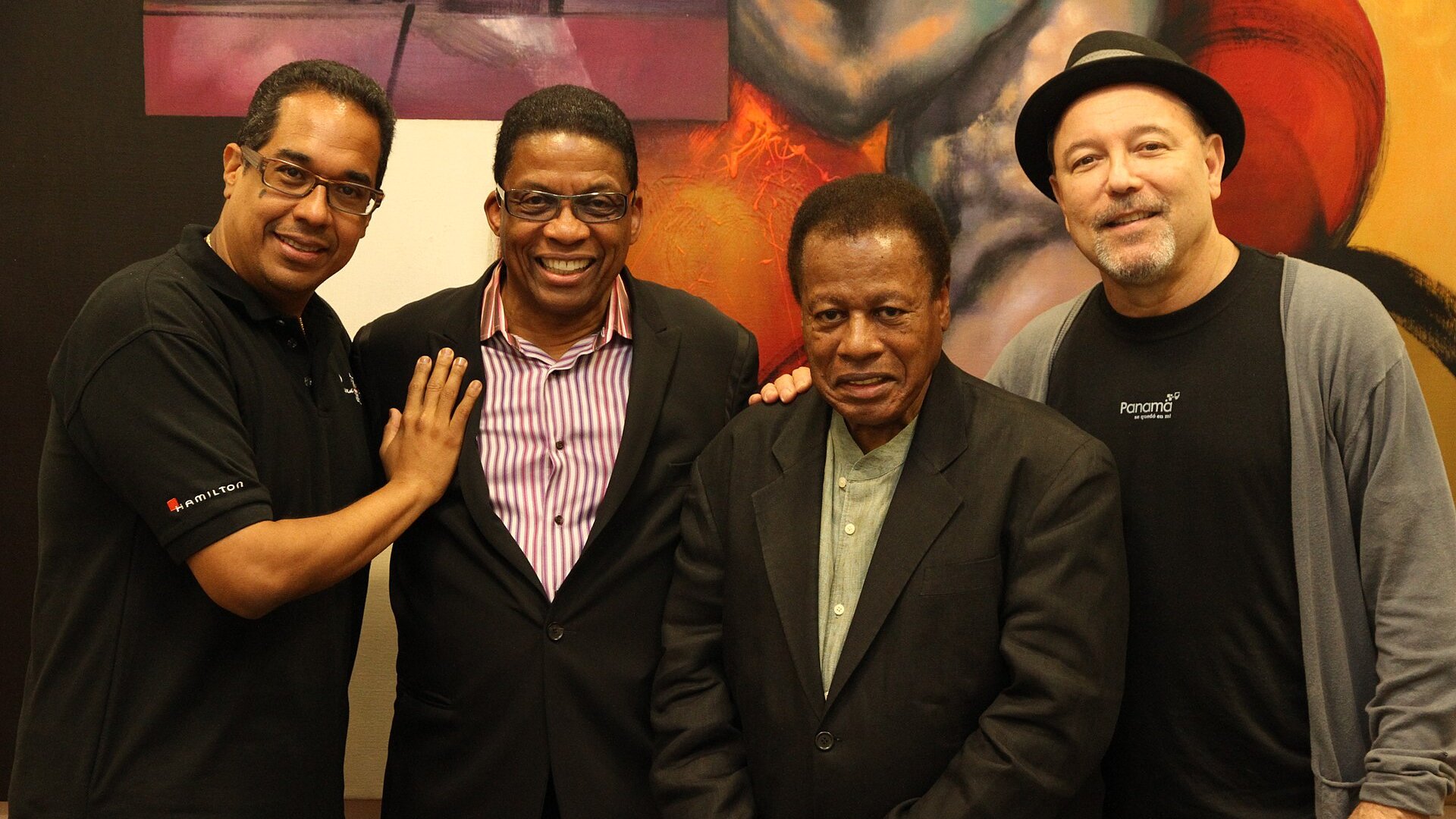 Four smiling musicians standing together in front of a colourful painting