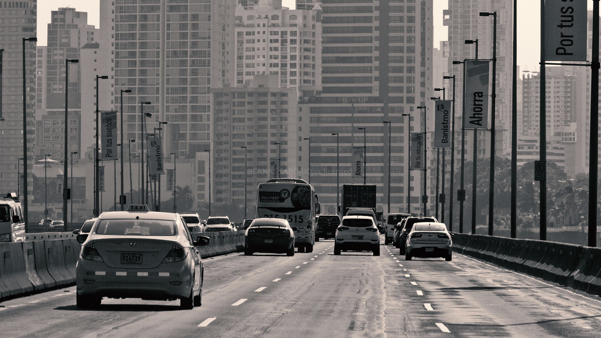 A taxi, a bus, a truck and cars drive along the Corredor Sur expressway in Panama City with high-rise towers behind