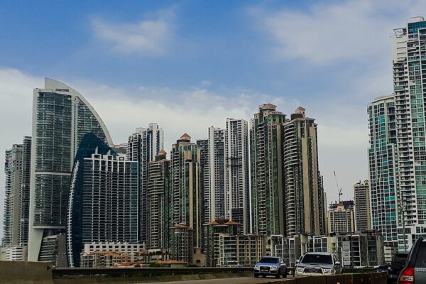 Tall residential and office towers of Panama City's Punta Pacifica district rise behind a highway, with cars in the foreground and a blue sky.