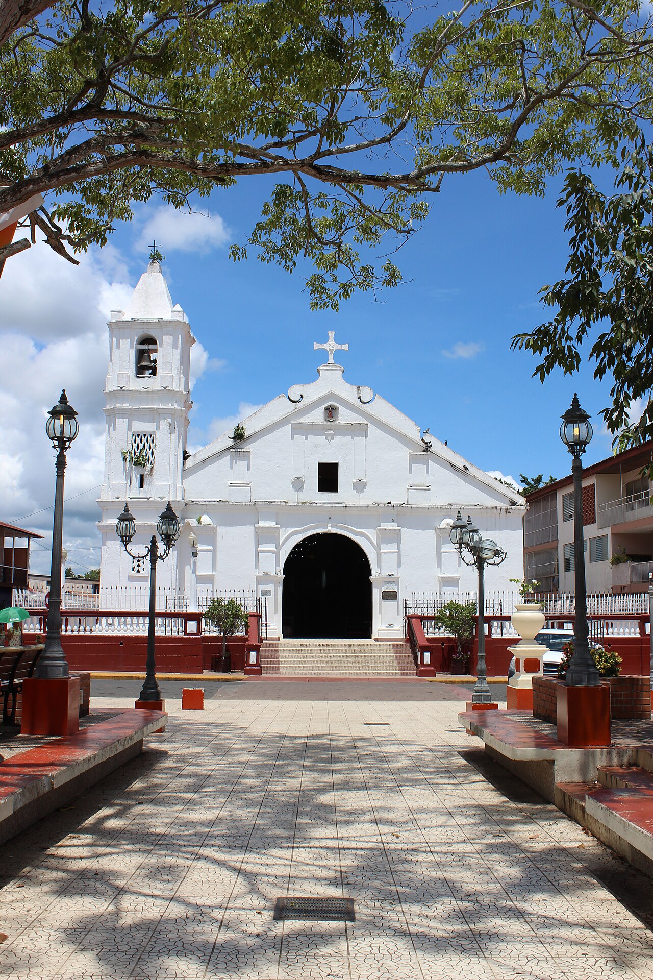 White colonial facade and bell tower of the Santa Librada parish church in Las Tablas, Panama, seen from the tiled square under a blue sky