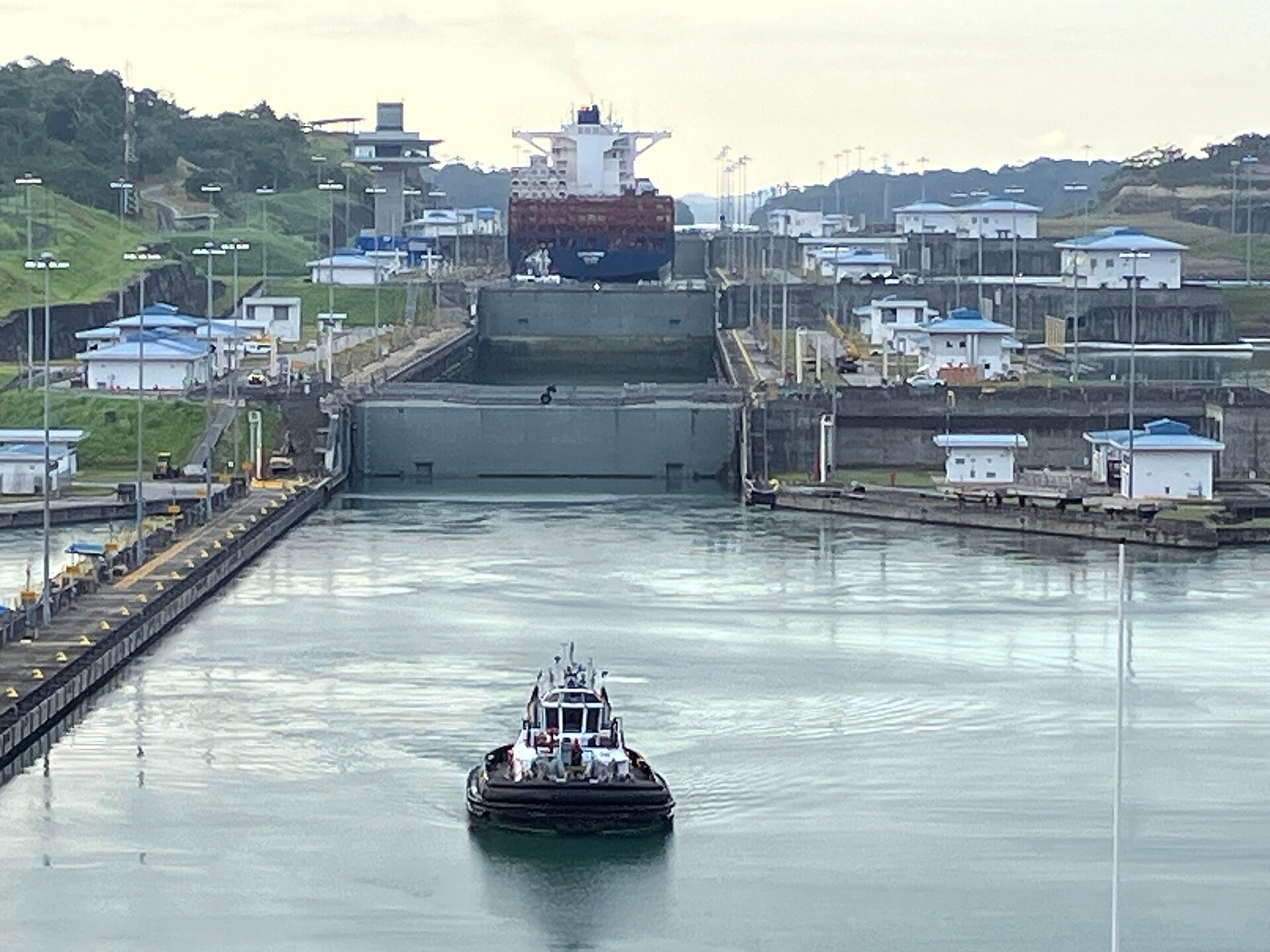 A tugboat guides a container ship into a lock of the Panama Canal in the early morning