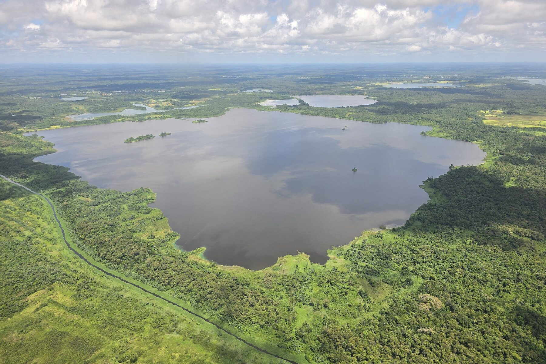 Aerial view of a large lake left by a worked-out bauxite mine in northern Para, Suriname, ringed by green forest and savannah, with a straight track running along its western edge