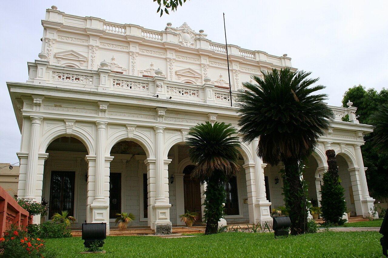 White neoclassical building of the National University of Asunción behind a lawn and palm trees
